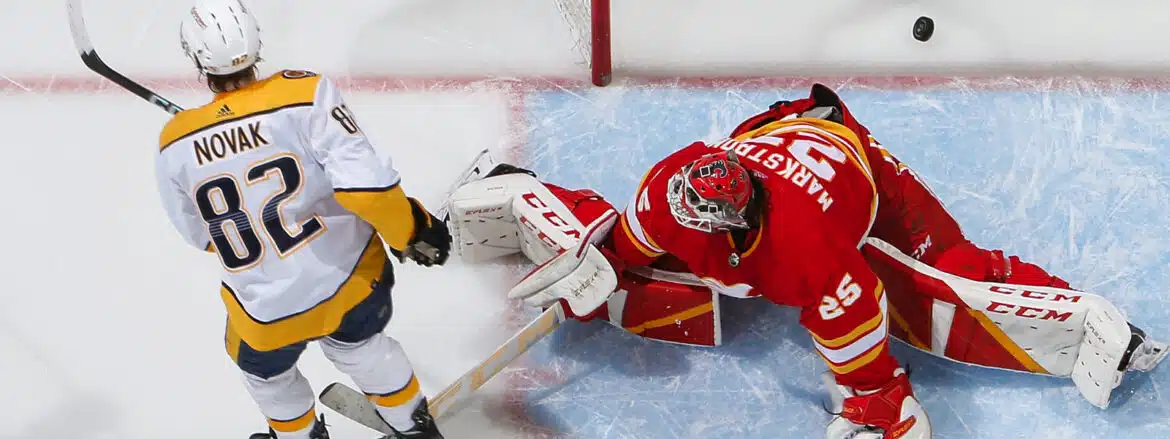 Hockey goalie in red gear making a save against an opponent.