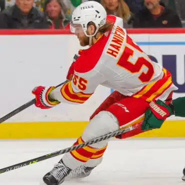 Ice hockey player in red and yellow uniform skating during a game.