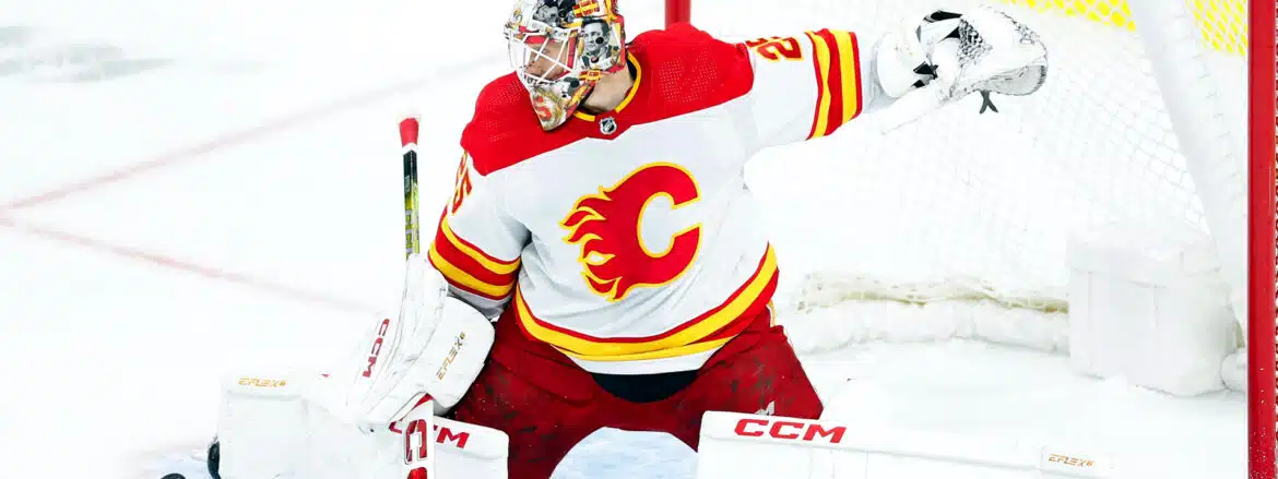 Hockey goalie in red and yellow Calgary Flames uniform making a save.