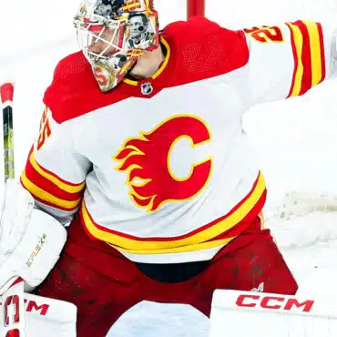 Hockey goalie in red and yellow Calgary Flames uniform making a save.