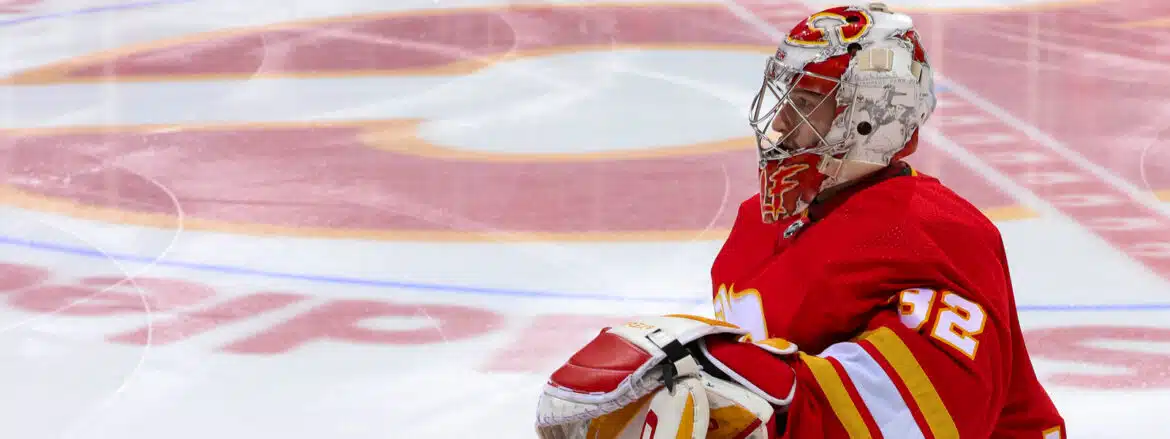 Ice hockey goalie in red and white gear guarding the net.