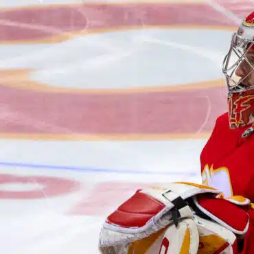 Ice hockey goalie in red and white gear guarding the net.