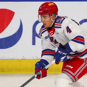 Hockey player in red and blue uniform skating on ice.