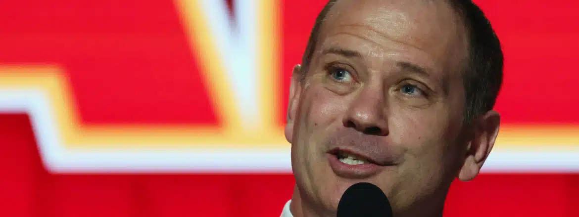 Man speaking into a microphone with a blurred red and yellow background.