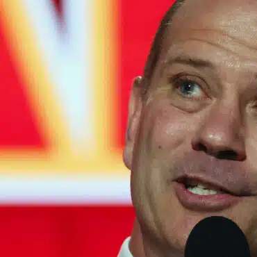 Man speaking into a microphone with a blurred red and yellow background.