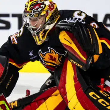 Ice hockey goalie in action wearing colorful gear.