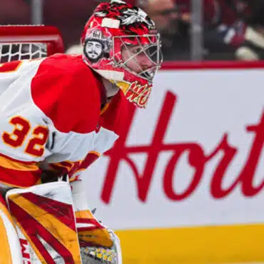 Hockey goalie in red and yellow gear focused during a game.
