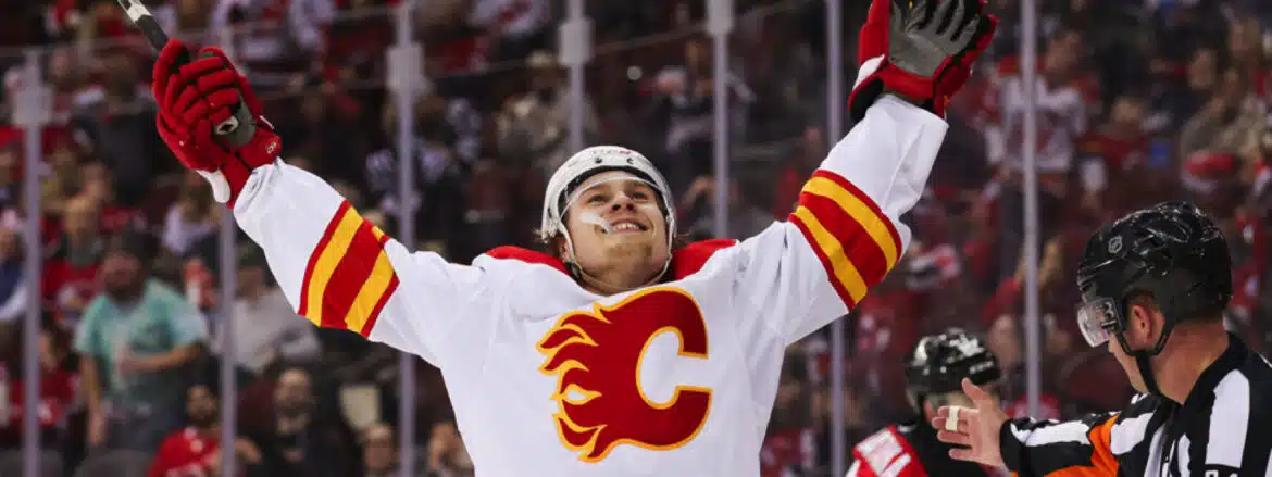 Hockey player in Calgary Flames jersey celebrates with arms raised.