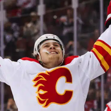 Hockey player in Calgary Flames jersey celebrates with arms raised.