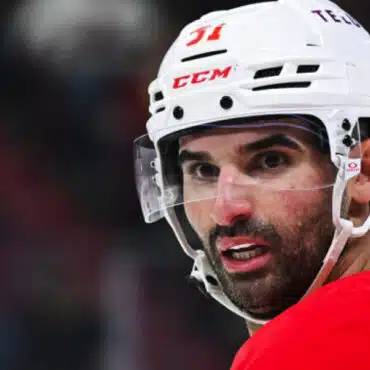 Close-up of a focused ice hockey player in a white helmet and red jersey.