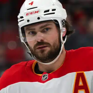 Close-up of a focused ice hockey player wearing a red and white jersey and helmet.