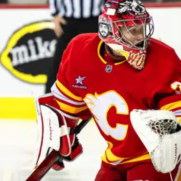 Ice hockey goalie in red Calgary Flames uniform ready to defend the goal.