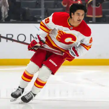 Ice hockey player in red and white Calgary Flames uniform skating on ice.