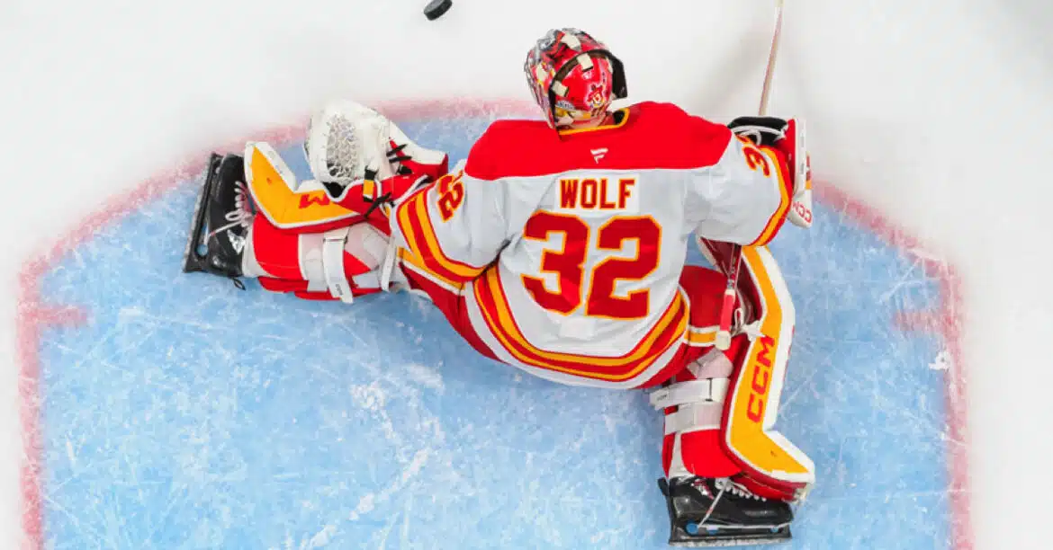 Hockey goalie in red and white gear sprawled on ice during a game.