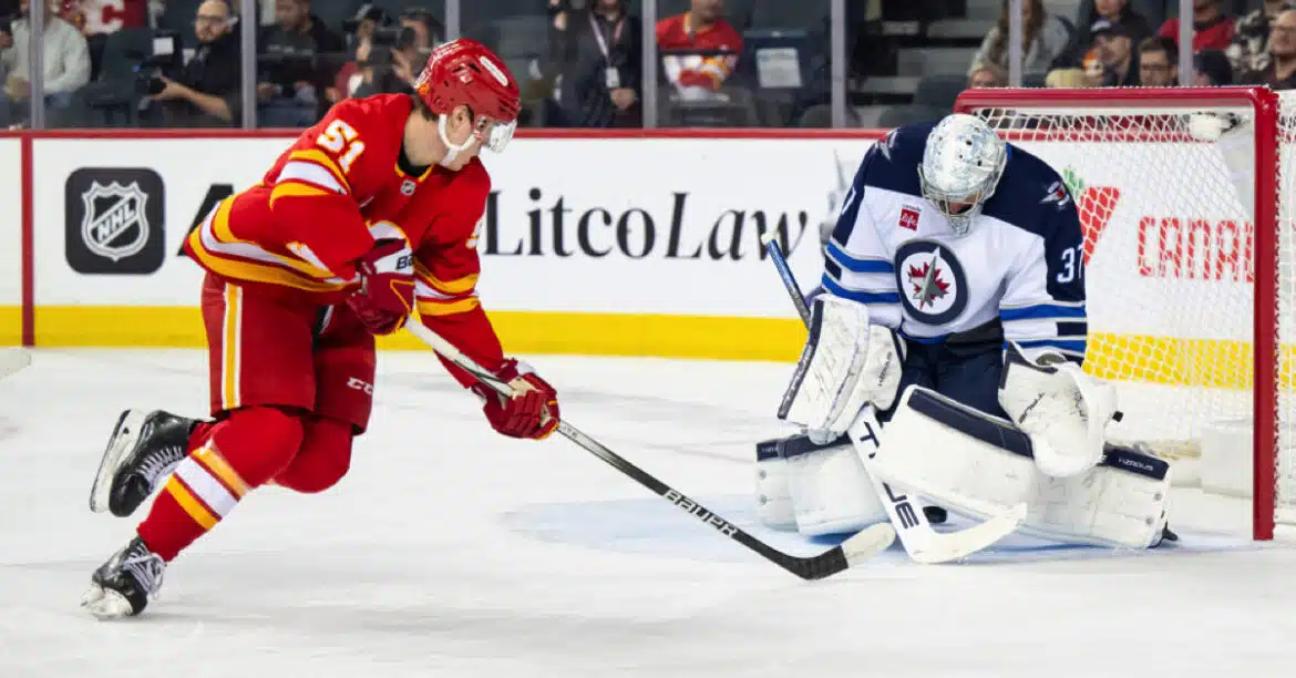 A hockey player in red shoots the puck past a goalie in white gear.