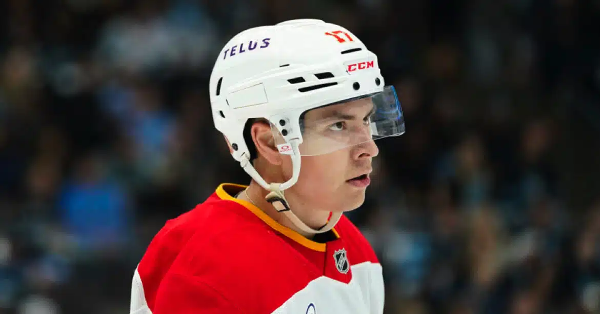 Ice hockey player in a white helmet and red jersey focused on the game.