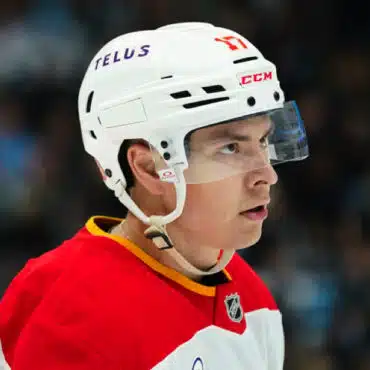 Ice hockey player in a white helmet and red jersey focused on the game.
