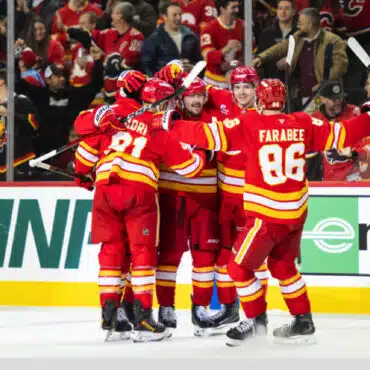 Hockey players in red uniforms celebrating a goal on ice.