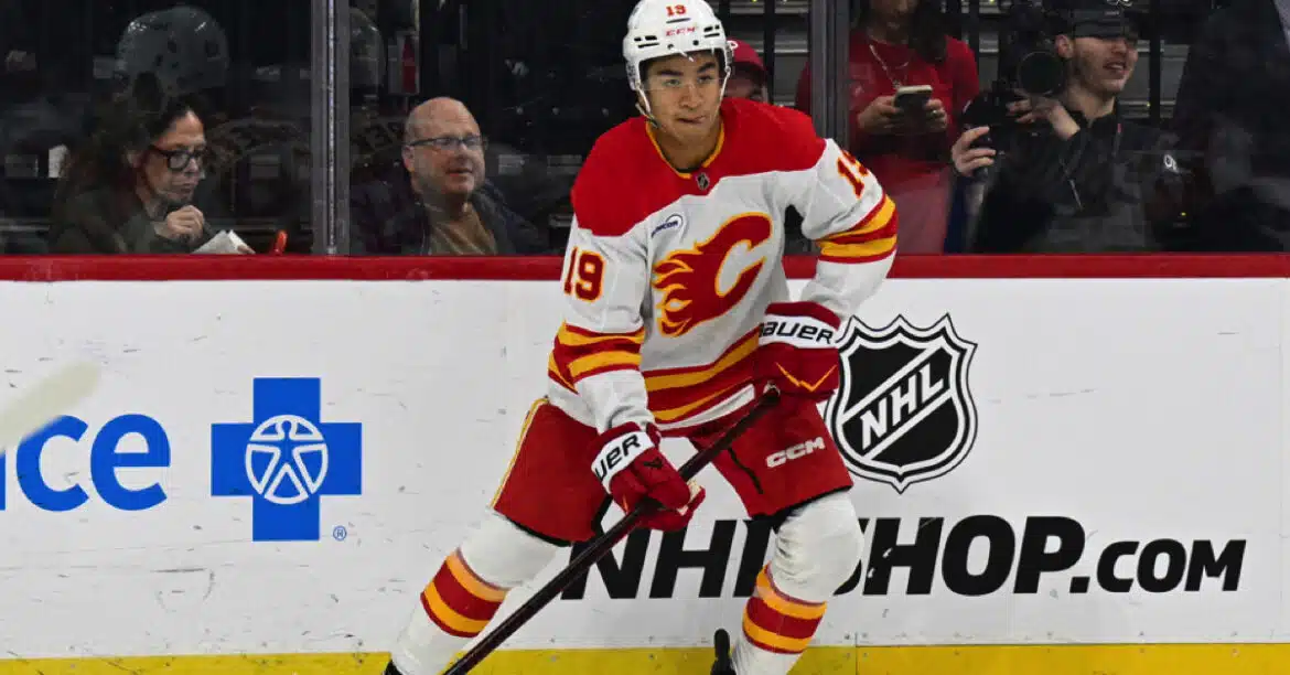 Hockey player in white and red Calgary Flames uniform skating on ice.