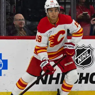 Hockey player in white and red Calgary Flames uniform skating on ice.
