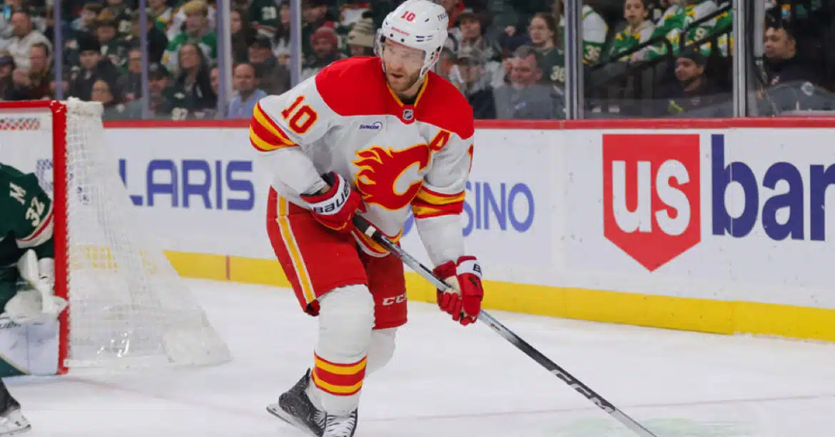 Hockey player in white and red Calgary Flames uniform skating with puck.