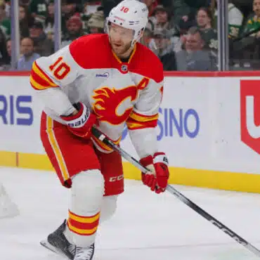 Hockey player in white and red Calgary Flames uniform skating with puck.