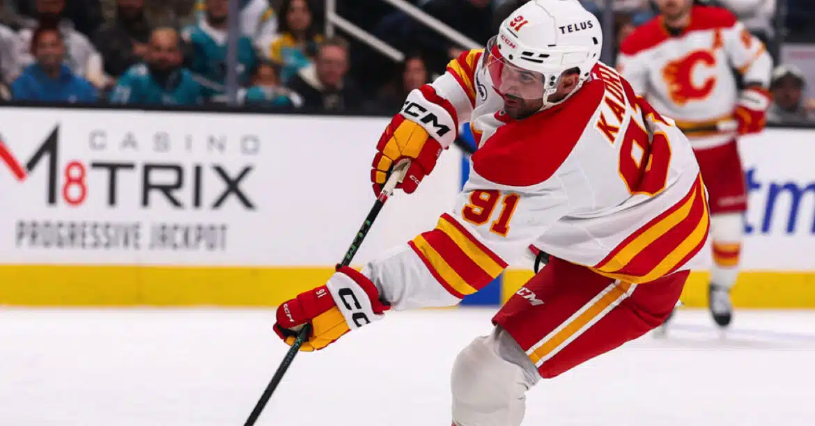 Hockey player in white and red uniform controlling the puck with a stick.