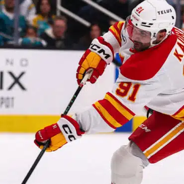 Hockey player in white and red uniform controlling the puck with a stick.