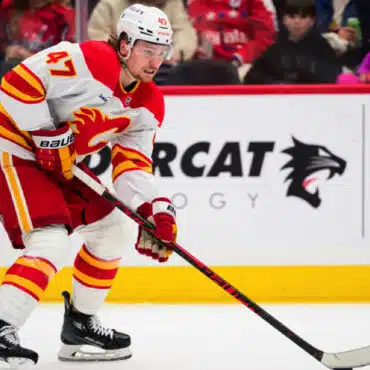 Hockey player in Calgary Flames uniform handling the puck on ice.