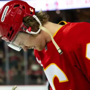 Hockey player in red jersey looking down thoughtfully on the ice.