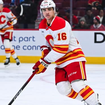 Hockey player in red and yellow uniform skating on ice with a stick.